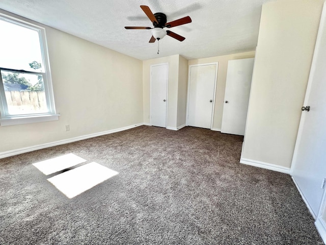 unfurnished bedroom with a textured ceiling, two closets, dark carpet, and ceiling fan