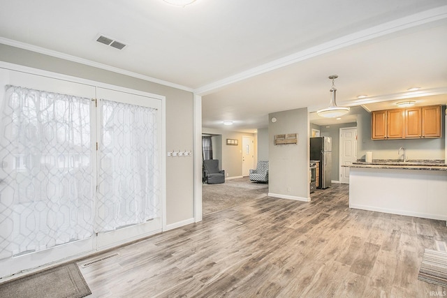 kitchen featuring crown molding, hanging light fixtures, light wood-type flooring, light stone countertops, and stainless steel refrigerator