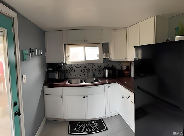 kitchen featuring white cabinets, decorative backsplash, and black fridge