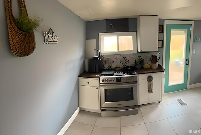 kitchen with white cabinets, light tile patterned flooring, high end range, and tasteful backsplash