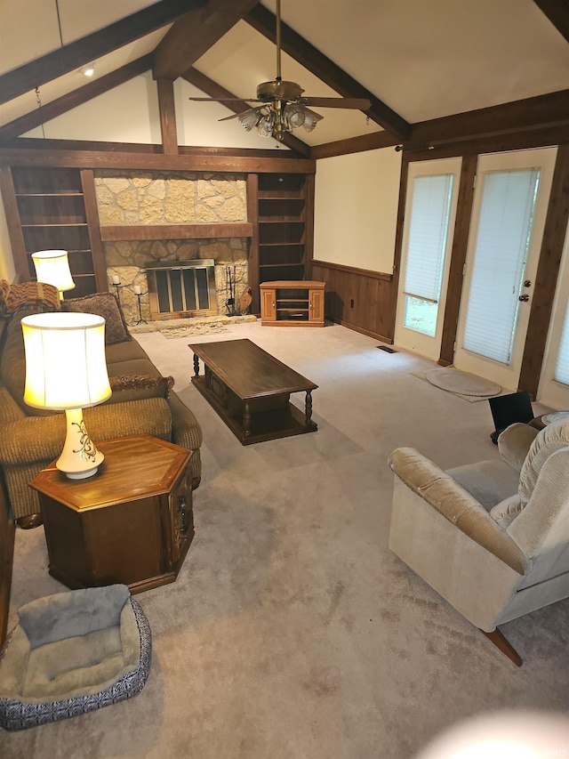 carpeted living room with lofted ceiling with beams, wooden walls, ceiling fan, built in features, and a fireplace