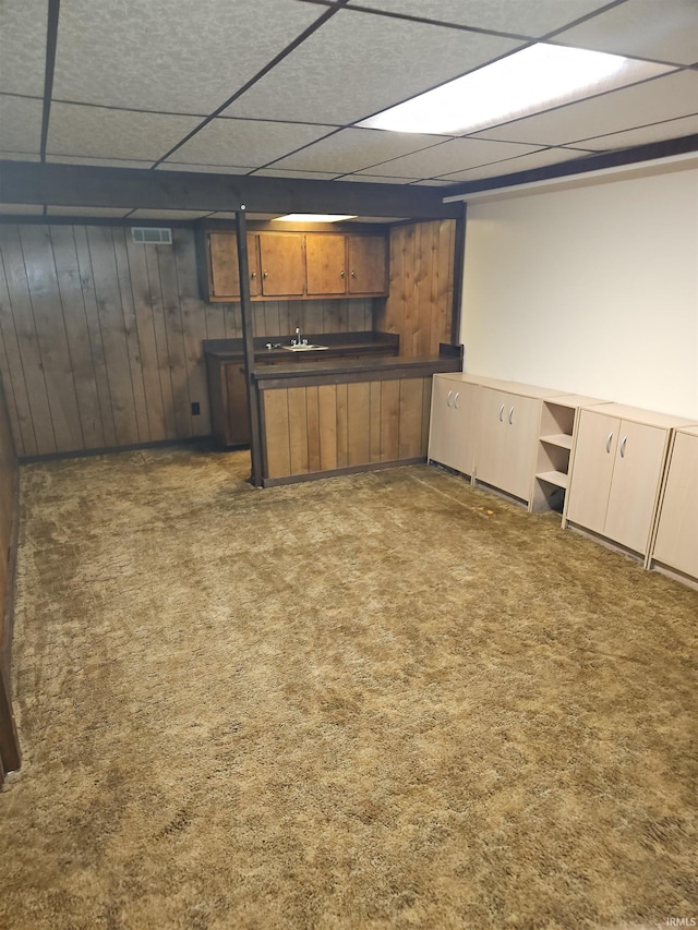 kitchen with dark colored carpet, a paneled ceiling, and wood walls