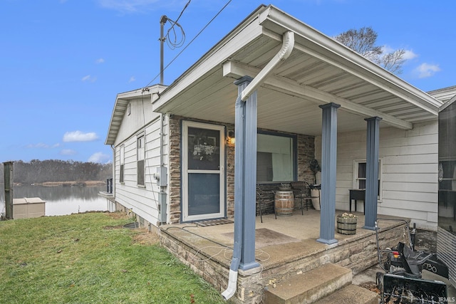 view of exterior entry featuring a lawn, covered porch, and a water view