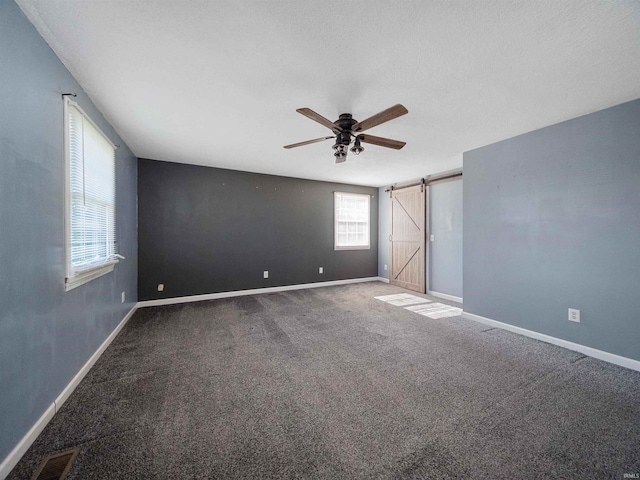 unfurnished room with a barn door, carpet floors, and ceiling fan