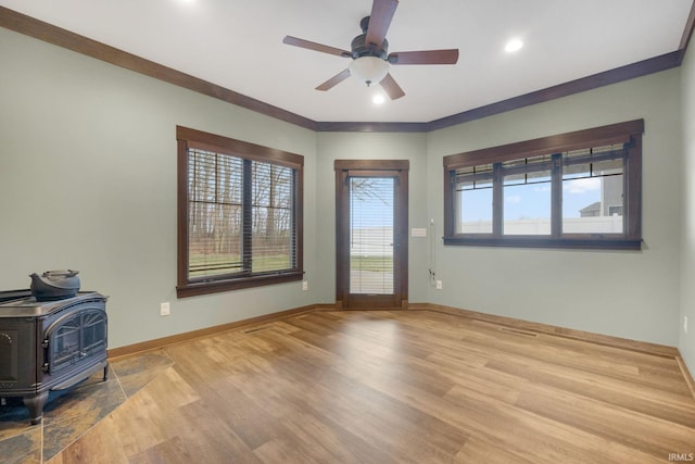 living room with ceiling fan, light hardwood / wood-style floors, a wood stove, and crown molding