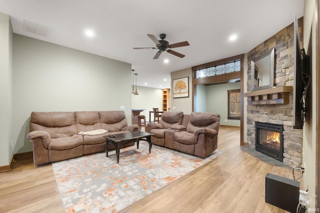 living room featuring light wood-type flooring, a stone fireplace, and ceiling fan