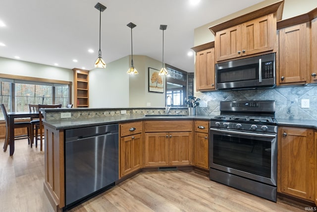 kitchen with kitchen peninsula, appliances with stainless steel finishes, light wood-type flooring, sink, and decorative light fixtures