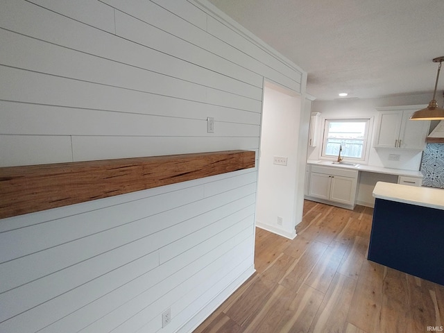 interior space featuring light wood-type flooring, wooden walls, sink, white cabinets, and hanging light fixtures