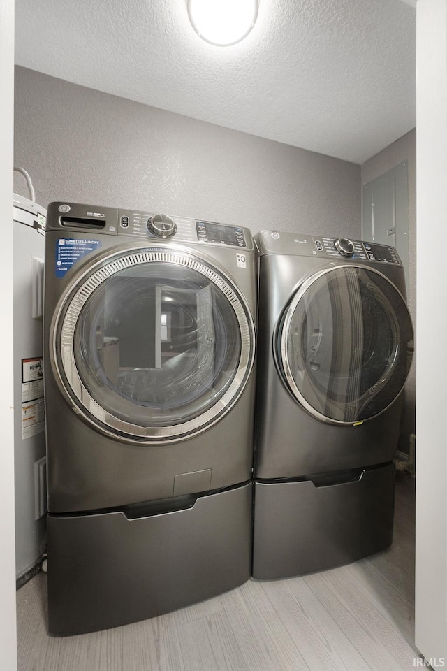 washroom with light hardwood / wood-style floors, a textured ceiling, and independent washer and dryer