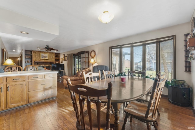 dining area with ceiling fan, dark hardwood / wood-style floors, and a brick fireplace