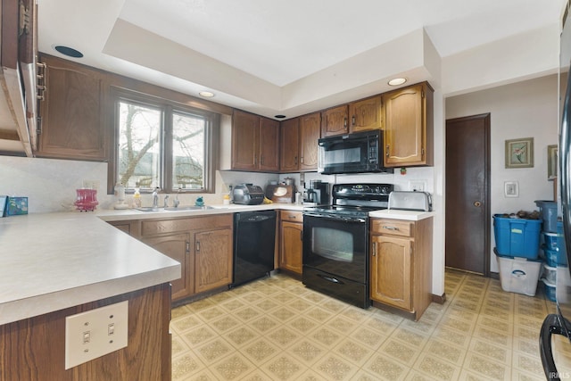 kitchen featuring sink, kitchen peninsula, a tray ceiling, decorative backsplash, and black appliances