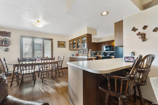 kitchen with black appliances, dark hardwood / wood-style floors, a kitchen bar, and kitchen peninsula