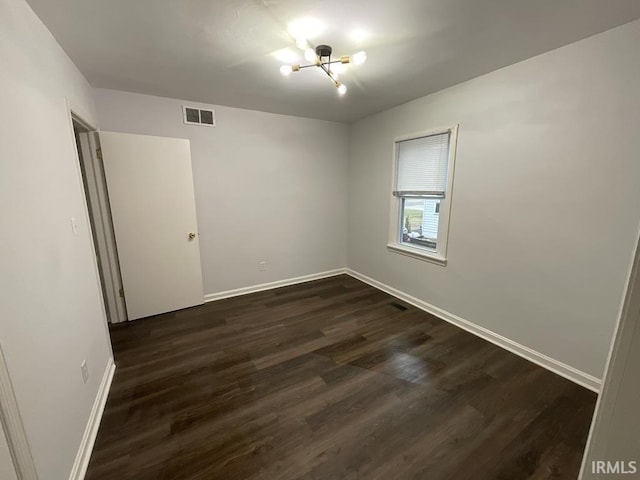 empty room featuring dark wood-type flooring and an inviting chandelier