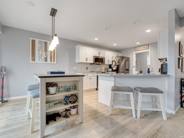 kitchen featuring kitchen peninsula, appliances with stainless steel finishes, decorative backsplash, white cabinets, and light wood-type flooring