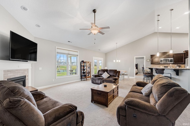 living room with ceiling fan with notable chandelier, light colored carpet, a fireplace, and high vaulted ceiling