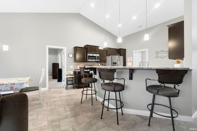 kitchen featuring dark brown cabinetry, stainless steel appliances, high vaulted ceiling, decorative light fixtures, and a breakfast bar area