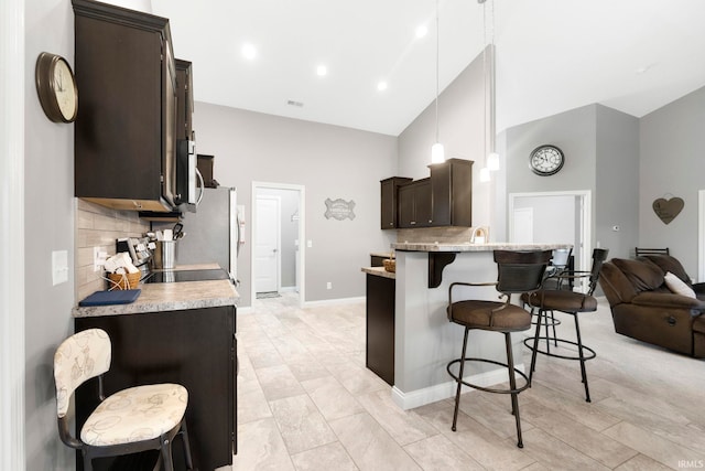 kitchen featuring a kitchen bar, decorative backsplash, dark brown cabinets, stainless steel appliances, and high vaulted ceiling