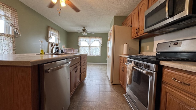 kitchen featuring sink, a textured ceiling, light tile patterned floors, appliances with stainless steel finishes, and ceiling fan