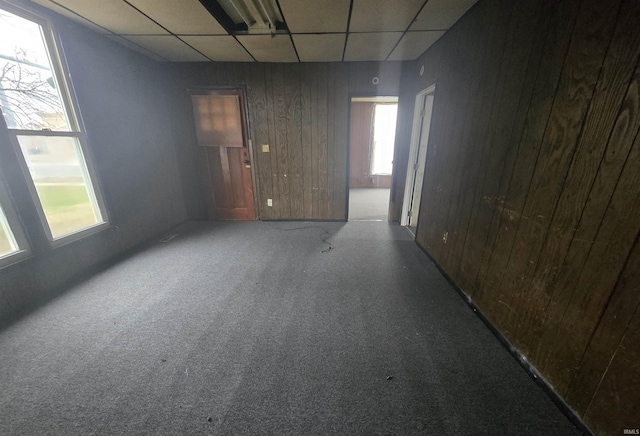 carpeted empty room with a drop ceiling and wood walls