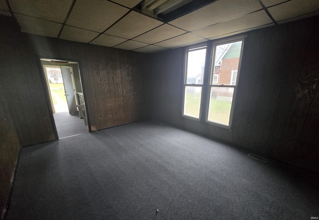 carpeted empty room with a drop ceiling and wood walls