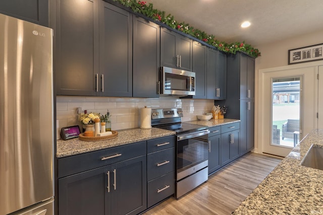 kitchen featuring backsplash, light stone countertops, light hardwood / wood-style floors, and appliances with stainless steel finishes