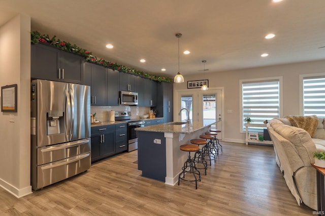 kitchen featuring a center island with sink, light stone countertops, appliances with stainless steel finishes, decorative light fixtures, and a breakfast bar area