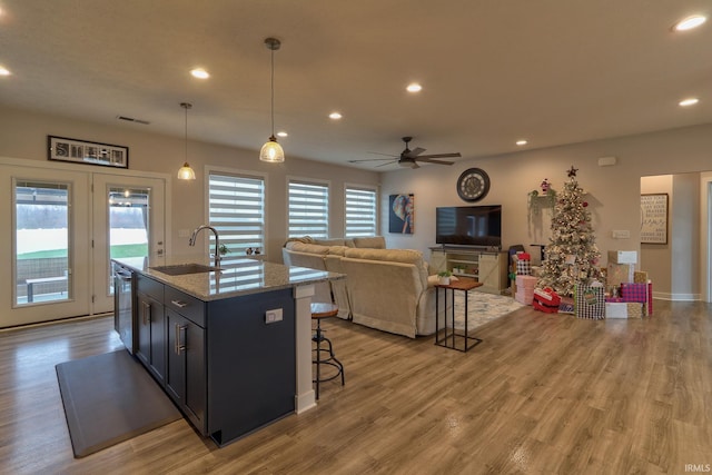 kitchen with light stone countertops, stainless steel dishwasher, pendant lighting, a kitchen bar, and a center island with sink