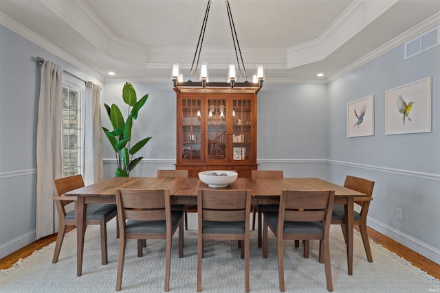 dining area featuring ornamental molding, light hardwood / wood-style floors, a chandelier, and a tray ceiling