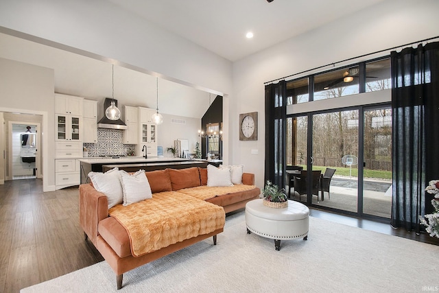 living room with hardwood / wood-style flooring, sink, high vaulted ceiling, and a chandelier