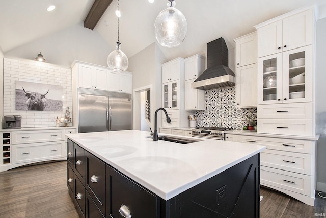 kitchen featuring high quality appliances, a center island with sink, wall chimney range hood, decorative light fixtures, and beam ceiling