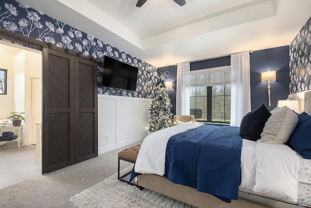 bedroom featuring a tray ceiling, a barn door, ceiling fan, and light colored carpet