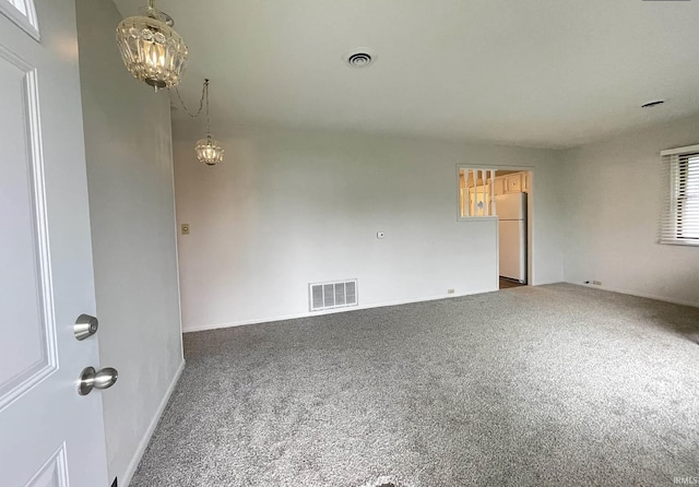 carpeted empty room with a healthy amount of sunlight and an inviting chandelier