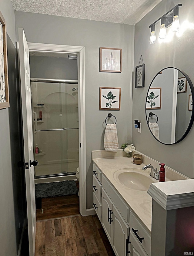 bathroom with toilet, a stall shower, a textured ceiling, wood finished floors, and vanity