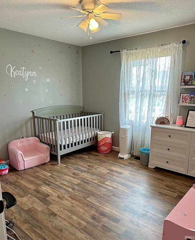 bedroom featuring ceiling fan, a nursery area, wood finished floors, and a textured ceiling