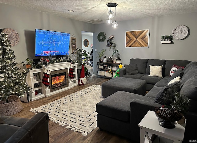 living area with visible vents, a textured ceiling, a warm lit fireplace, and wood finished floors