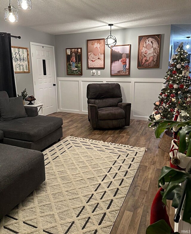 living room with a decorative wall, a textured ceiling, a wainscoted wall, and wood finished floors