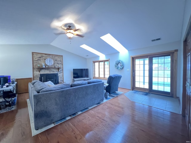 living room featuring vaulted ceiling with skylight, ceiling fan, hardwood / wood-style floors, and a brick fireplace