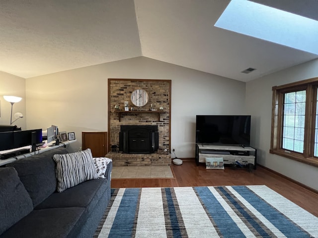 living room with a wood stove, vaulted ceiling with skylight, and dark wood-type flooring