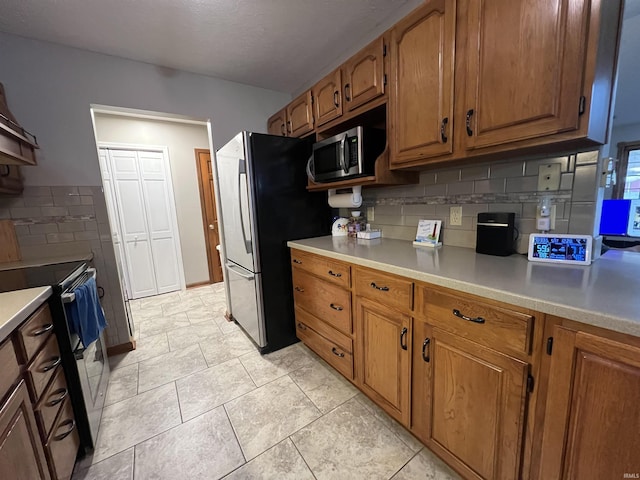 kitchen featuring backsplash, light tile patterned floors, and stainless steel appliances