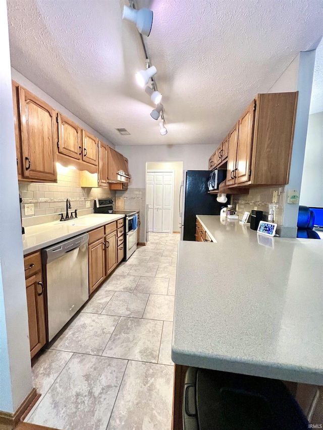 kitchen with decorative backsplash, kitchen peninsula, rail lighting, stainless steel appliances, and sink