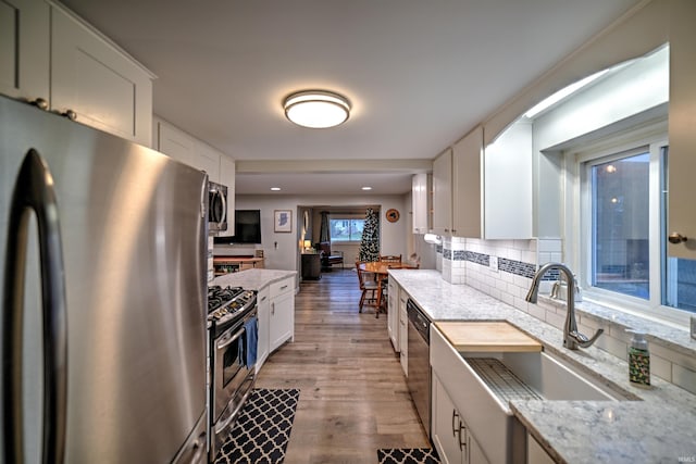 kitchen with light stone countertops, white cabinetry, sink, stainless steel appliances, and decorative backsplash