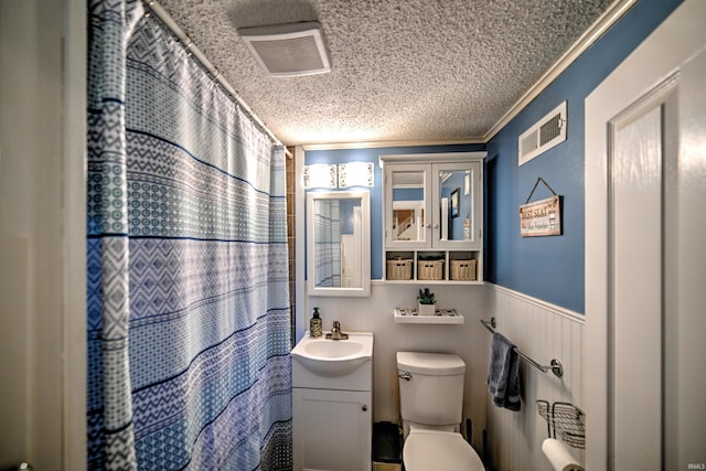 bathroom featuring vanity, wooden walls, toilet, ornamental molding, and a textured ceiling