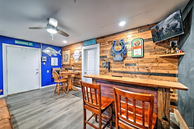 bar with ceiling fan, hardwood / wood-style floors, and wood walls