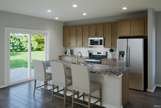 kitchen featuring dark wood-type flooring, sink, appliances with stainless steel finishes, and an island with sink