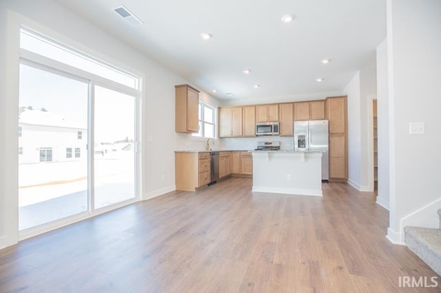 kitchen with appliances with stainless steel finishes, a kitchen island, sink, backsplash, and light wood-type flooring