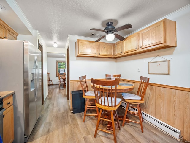 dining room with baseboard heating, wood walls, crown molding, and light wood-type flooring