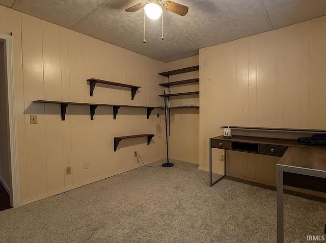 basement featuring ceiling fan, wood walls, and light carpet