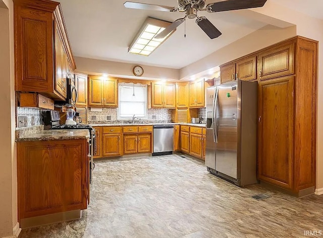 kitchen with sink, ceiling fan, appliances with stainless steel finishes, tasteful backsplash, and light stone counters