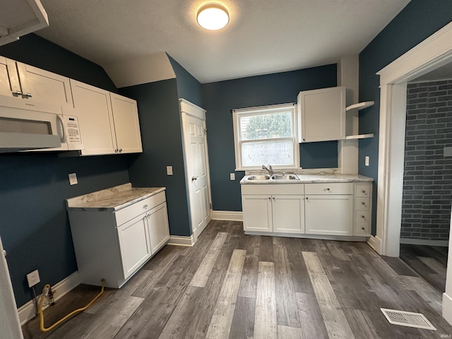 kitchen featuring dark hardwood / wood-style flooring, brick wall, a textured ceiling, sink, and white cabinetry