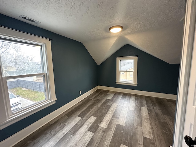 additional living space featuring hardwood / wood-style floors, plenty of natural light, a textured ceiling, and vaulted ceiling